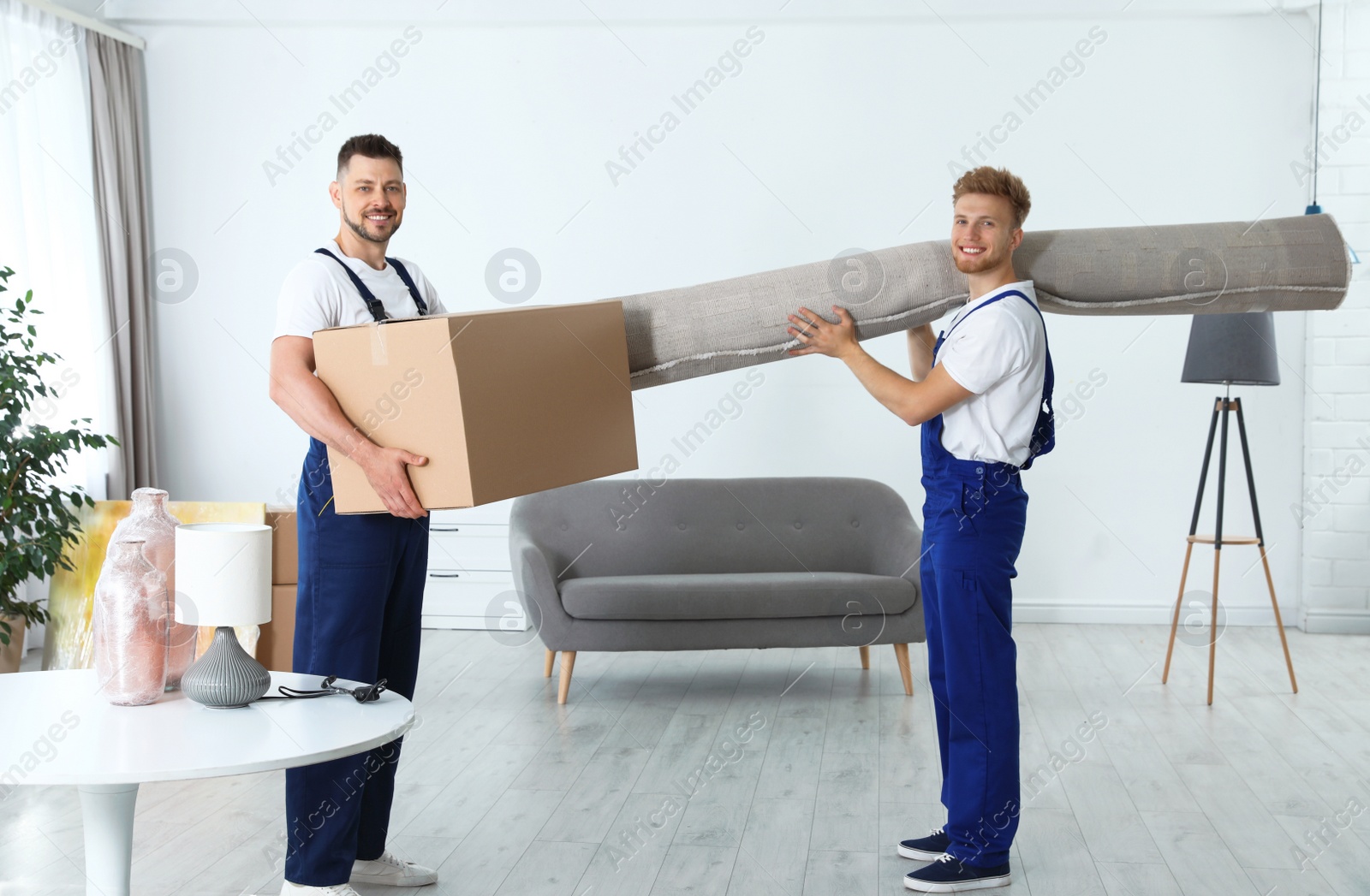 Photo of Moving service employees with box and carpet in room