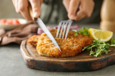Photo of Woman eating delicious schnitzel with microgreens and lemon at grey table, closeup