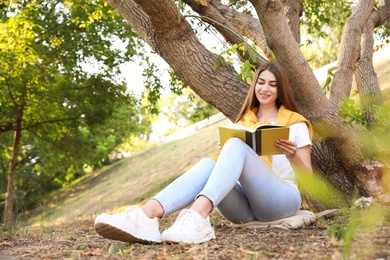 Photo of Young woman reading book near tree in park