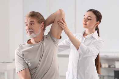 Professional orthopedist examining patient's shoulder in clinic