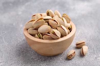 Delicious pistachios in bowl on grey textured table