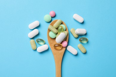 Photo of Different vitamin pills in wooden spoon on light blue background, top view