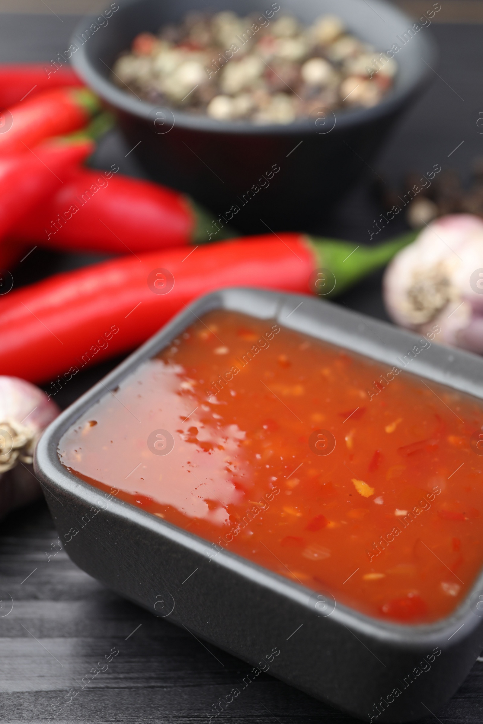 Photo of Spicy chili sauce in bowl on black wooden table, closeup