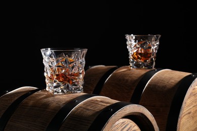 Photo of Tasty whiskey on wooden barrels against black background