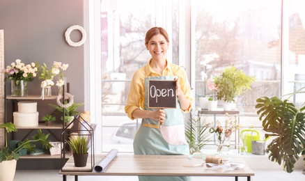 Photo of Female florist holding OPEN sign at workplace