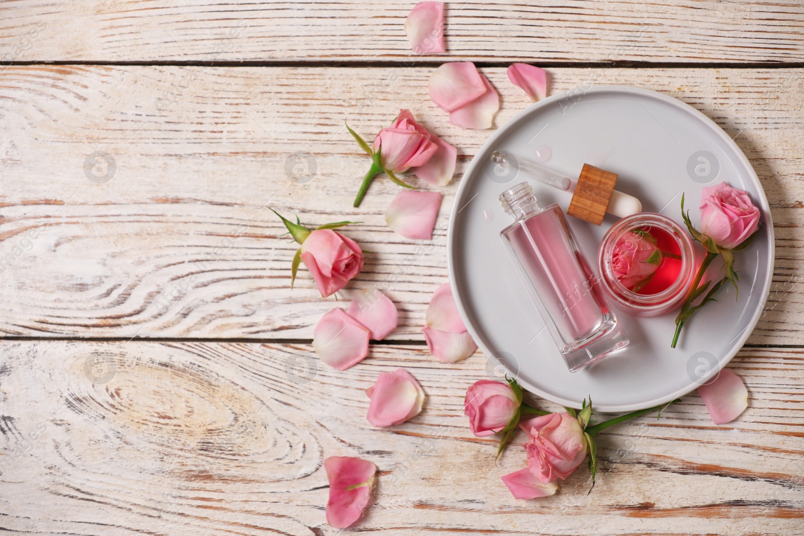 Photo of Flat lay composition with essential rose oil and flowers on white wooden table. Space for text