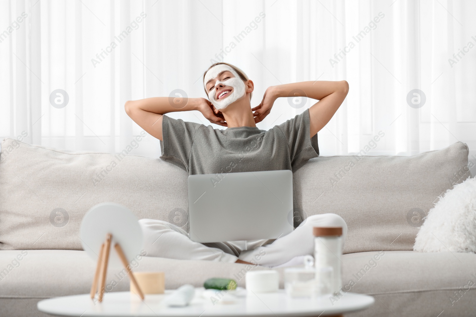 Photo of Young woman with face mask using laptop on sofa at home. Spa treatments