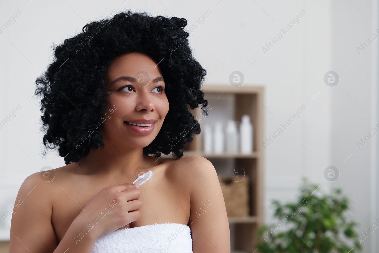 Photo of Young woman applying cream onto body indoors. Space for text