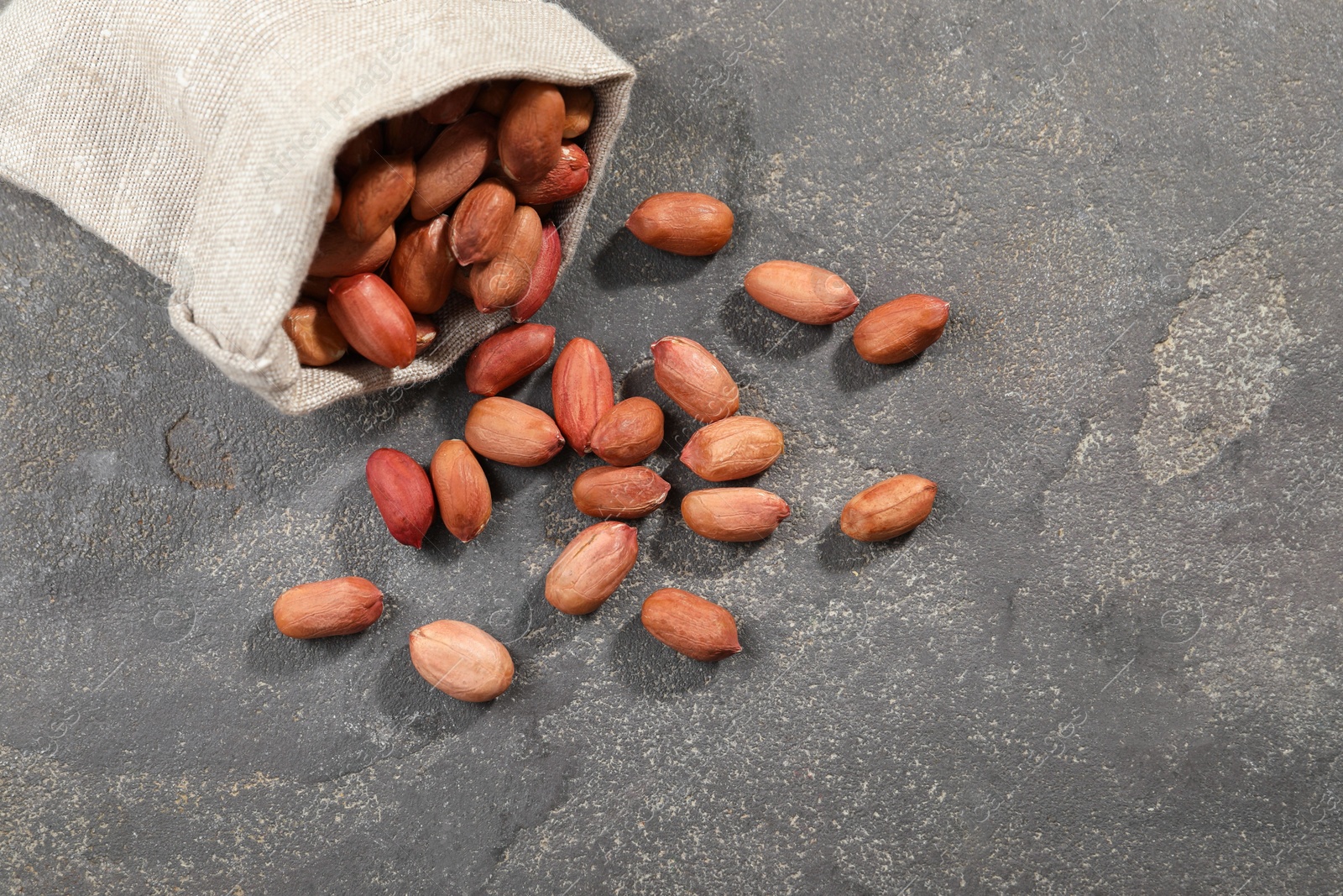 Photo of Fresh unpeeled peanuts and sack on grey table, space for text