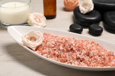 Photo of Natural sea salt in bowl, spa stones, roses and candle on wooden table