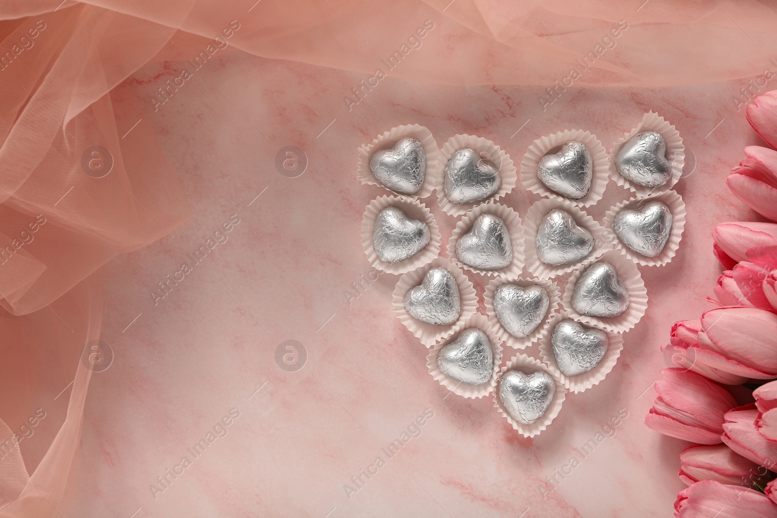 Photo of Heart made with delicious chocolate candies and beautiful tulips on pink table, flat lay. Space for text