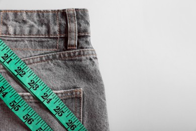 Photo of Jeans with measuring tape on light grey background, top view and space for text. Weight loss concept