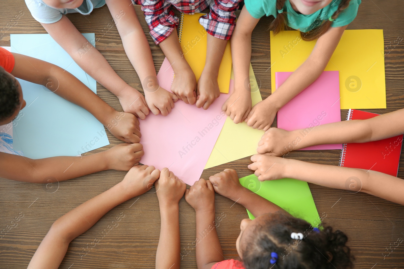 Photo of Little children putting their hands together at table, top view. Unity concept