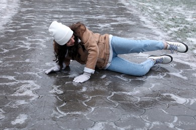 Photo of Young woman fallen on slippery icy pavement outdoors