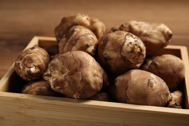 Photo of Crate with fresh Jerusalem artichokes on wooden table, closeup