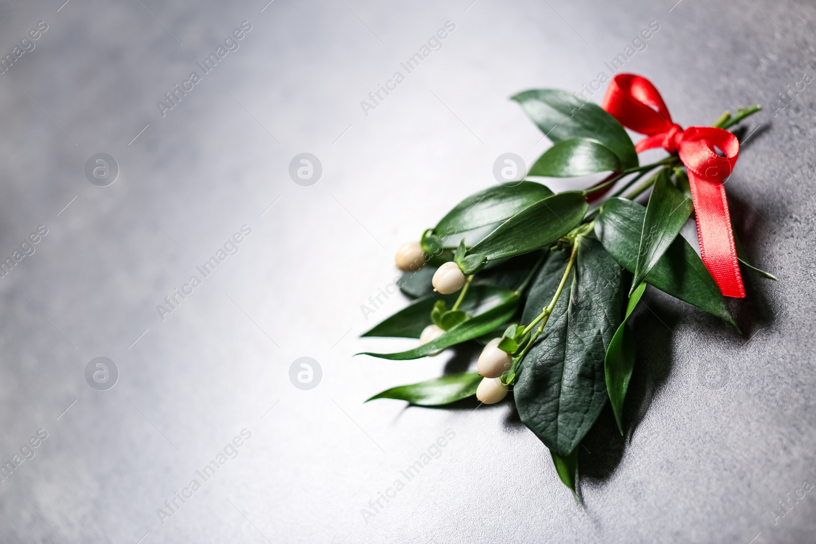 Photo of Mistletoe bunch with red bow and space for text on grey background, above view. Traditional Christmas decor