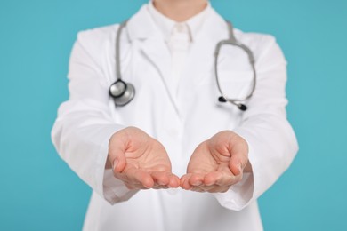 Photo of Doctor with stethoscope holding something on light blue background, closeup