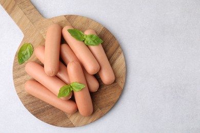 Photo of Delicious boiled sausages and basil on light gray table, top view. Space for text