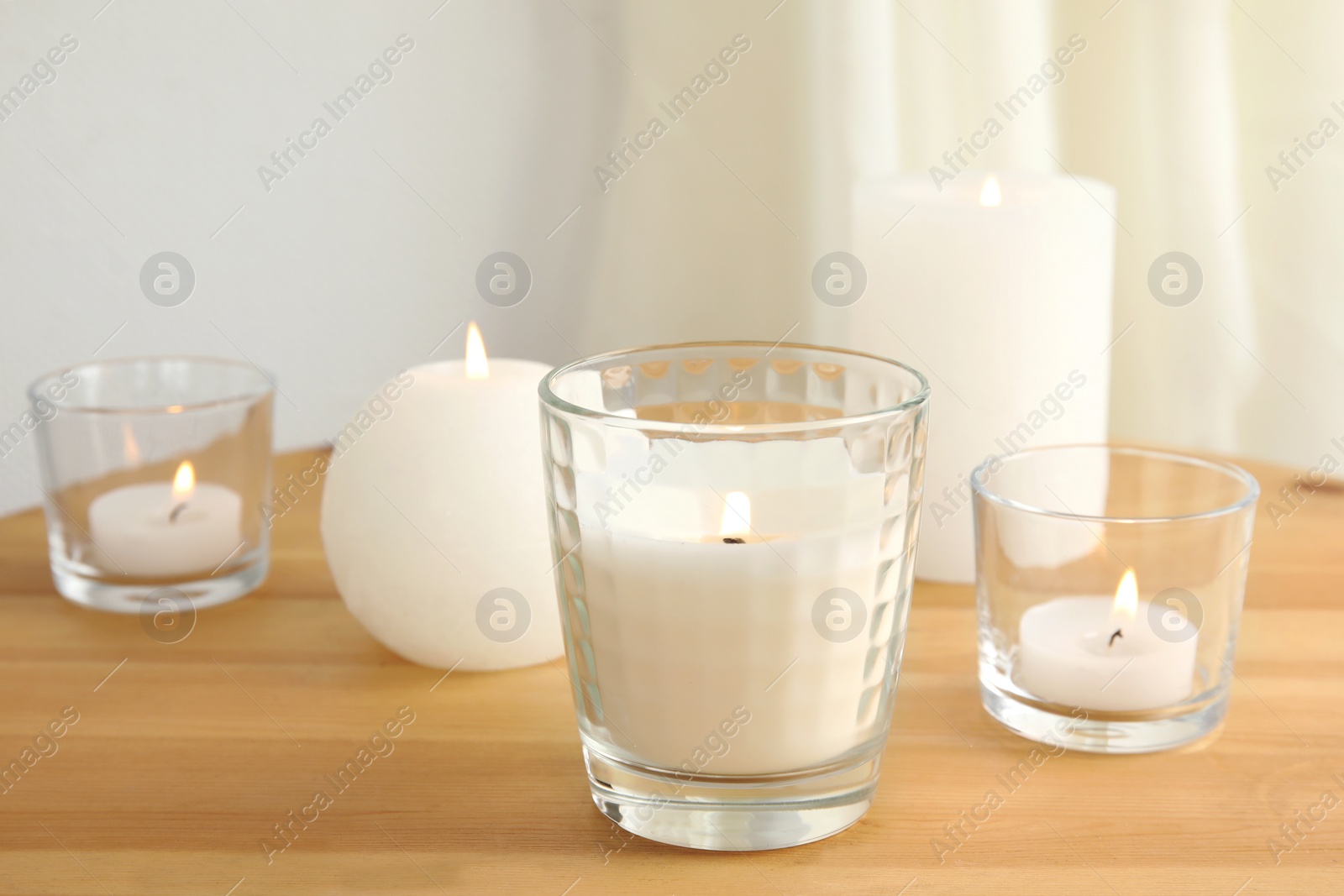 Photo of Different burning aromatic candles on wooden table