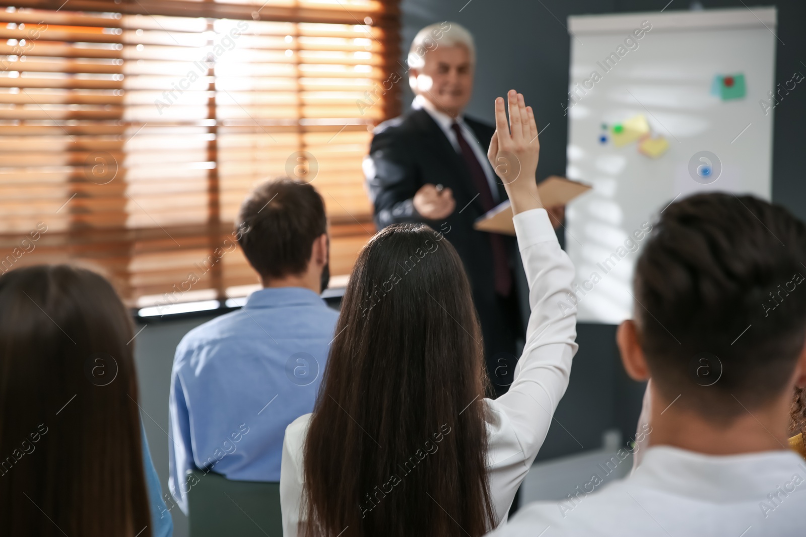 Photo of Woman raising hand to ask questions at seminar in office