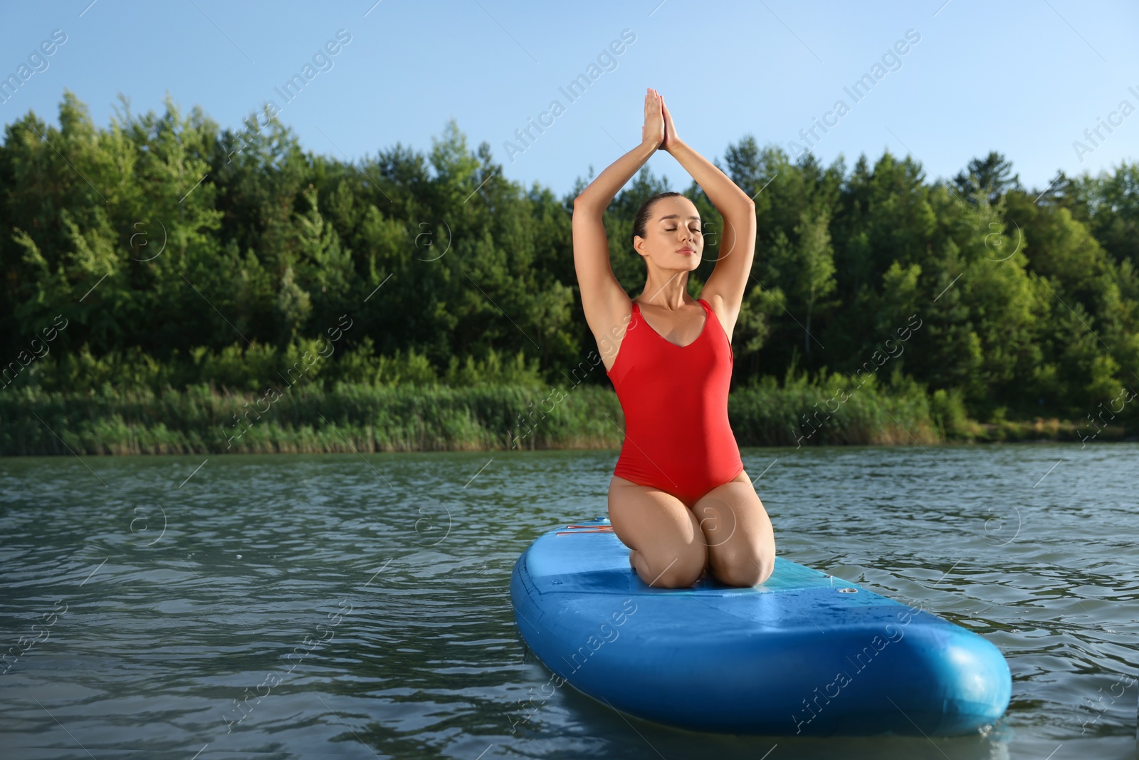 Photo of Young woman practicing yoga on light blue SUP board on river