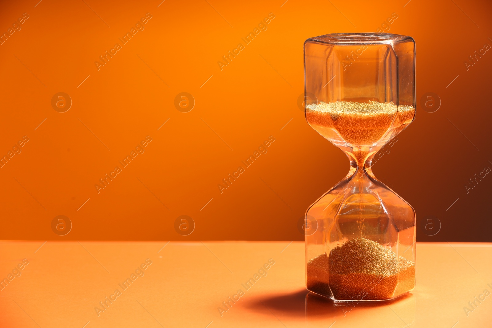 Photo of Hourglass with flowing sand on color background. Space for text