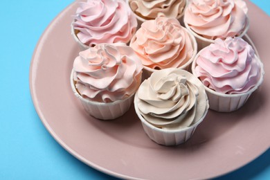 Photo of Plate with tasty cupcakes on light blue background, closeup