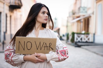 Photo of Sad woman in embroidered dress holding poster No War on city street. Space for text