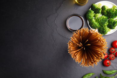 Uncooked buckwheat noodles and fresh ingredients on black table, flat lay. Space for text