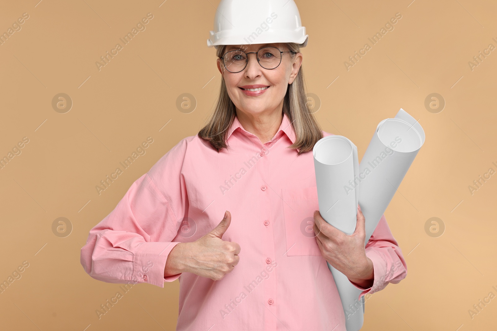 Photo of Architect in hard hat with drafts showing thumbs up on beige background