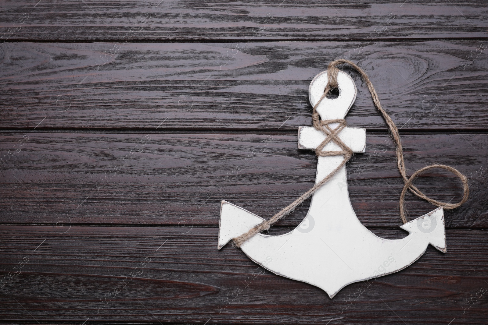 Photo of White anchor with hemp rope on dark wooden table, top view. Space for text