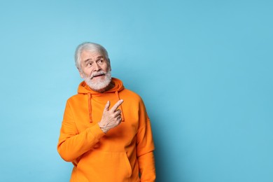 Photo of Senior man with mustache pointing at something on light blue background, space for text