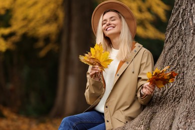 Happy woman with dry autumn leaves near tree outdoors. Space for text