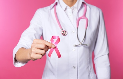 Photo of Female doctor with pink ribbon and stethoscope on color background, closeup. Breast cancer concept