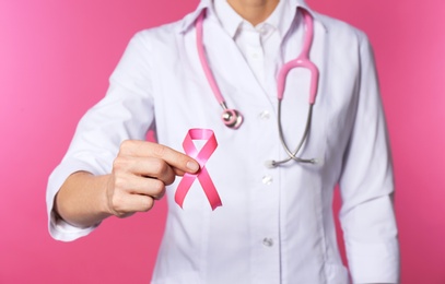 Female doctor with pink ribbon and stethoscope on color background, closeup. Breast cancer concept