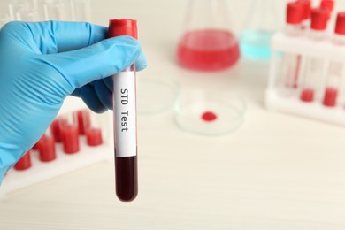 Scientist holding tube with blood sample and label STD Test on blurred background, closeup. Space for text