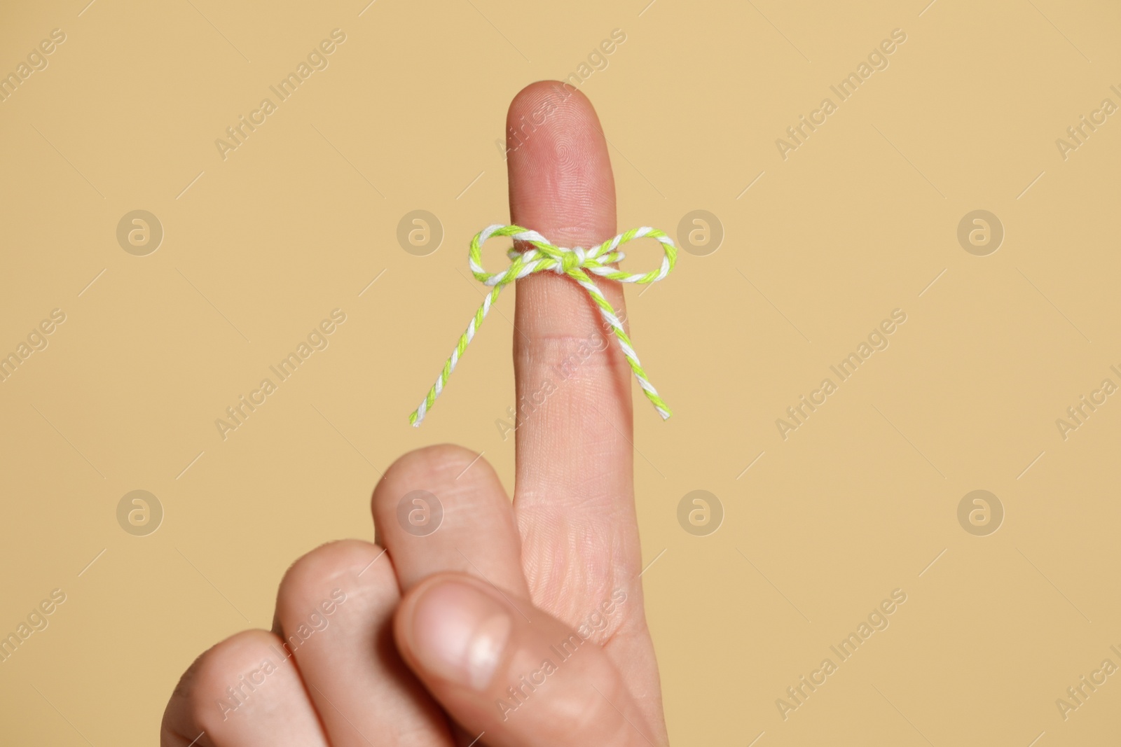 Photo of Man showing index finger with tied bow as reminder on beige background, closeup