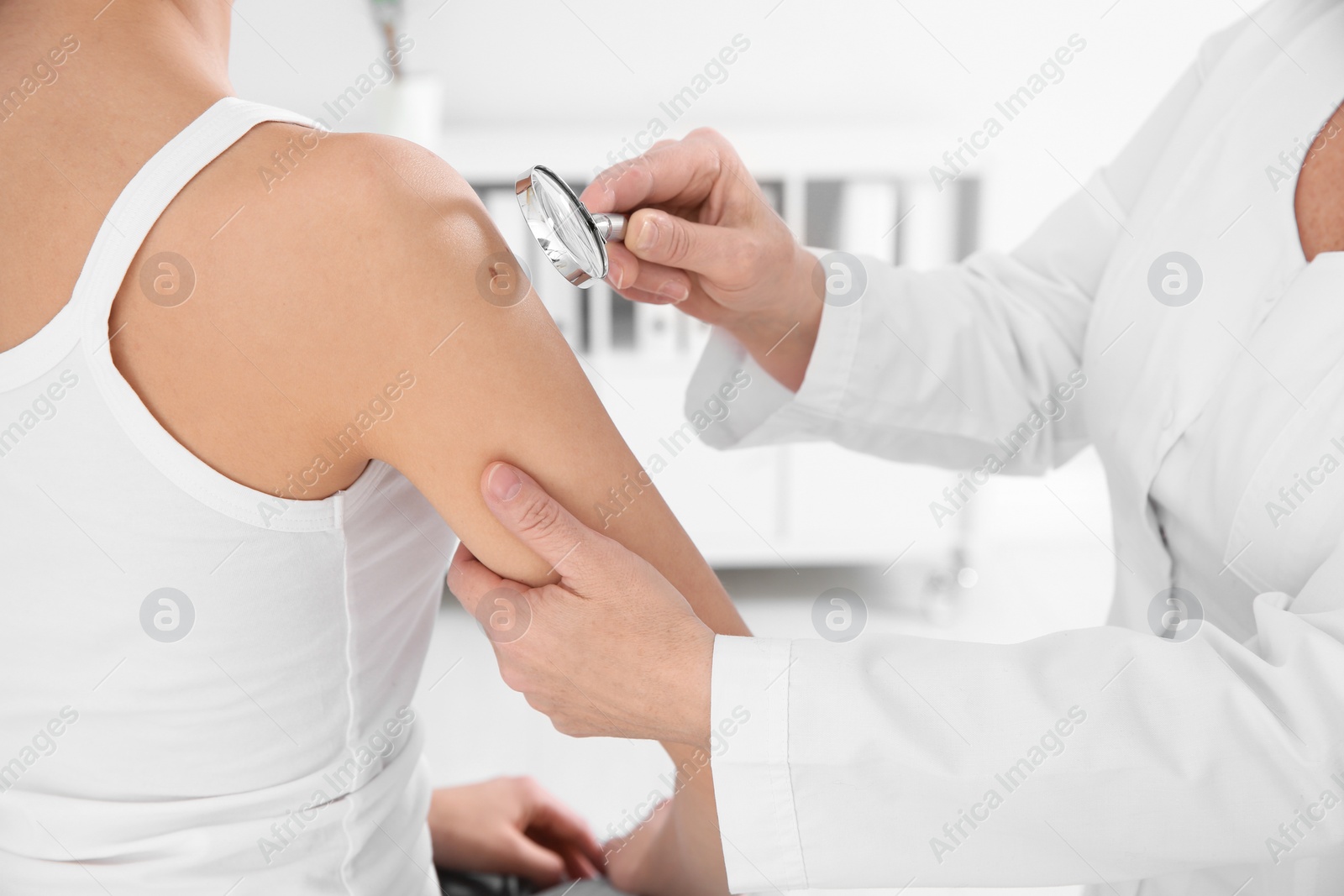 Photo of Dermatologist examining patient's birthmark with magnifying glass in clinic, closeup