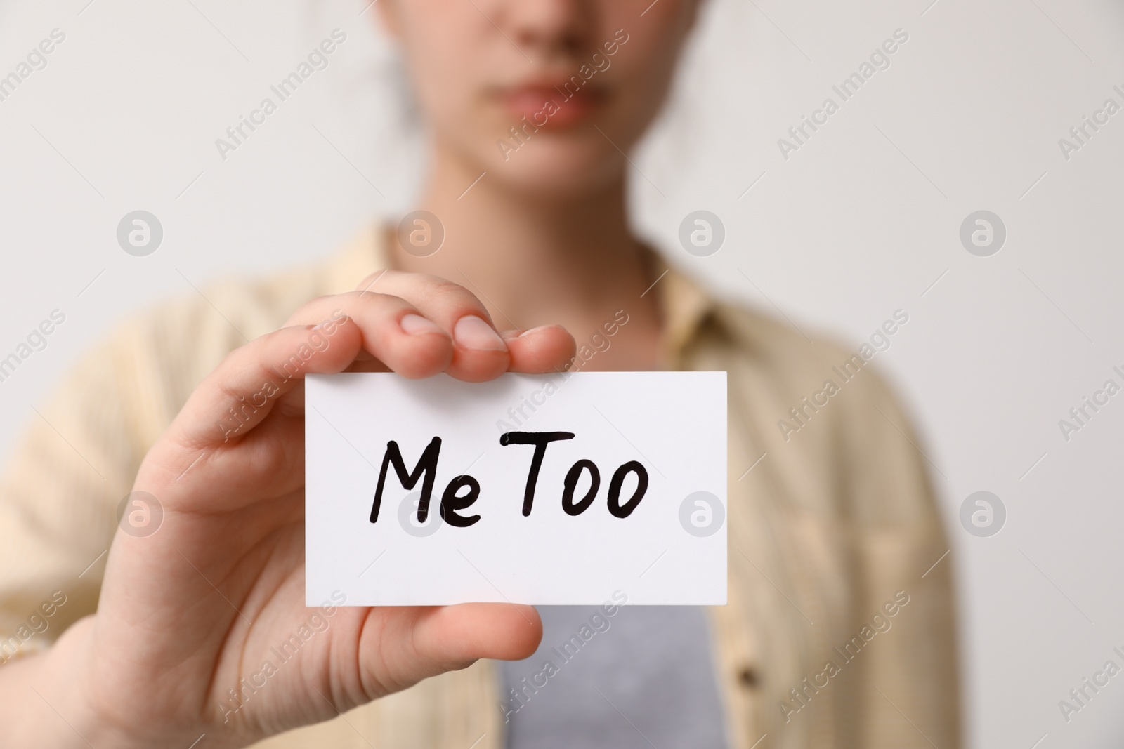 Photo of Woman holding paper with text MeToo against light background, closeup. Stop sexual assault