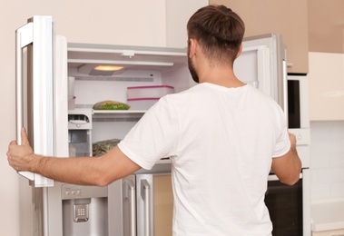 Photo of Young man searching for food in refrigerator at home