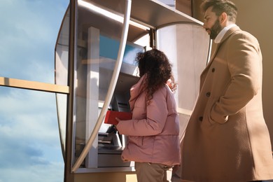 Photo of Young woman using modern cash machine outdoors. ATM queue