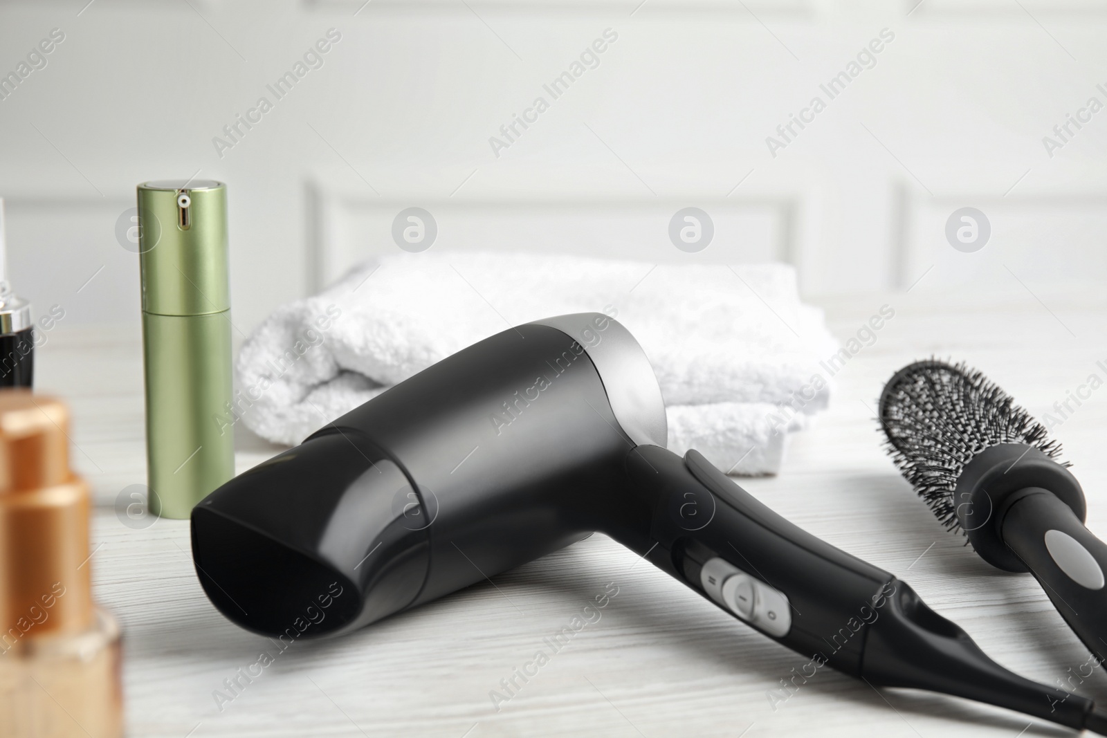 Photo of Hair care products, dryer and round brush on white wooden table, closeup