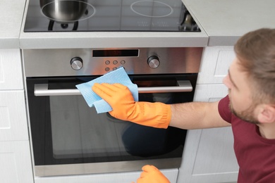 Photo of Young man cleaning oven with rag in kitchen