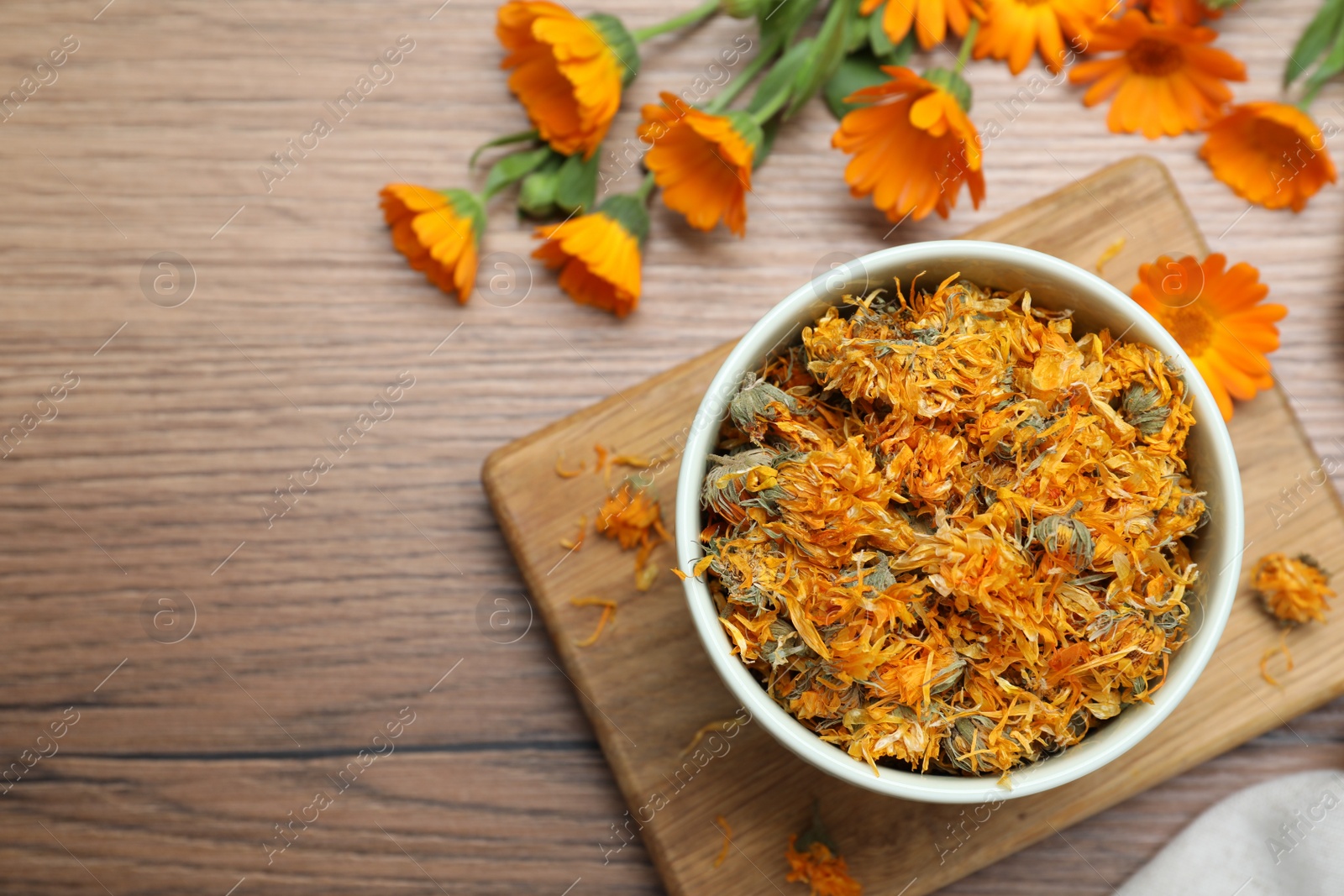 Photo of Dry and fresh calendula flowers on wooden table, flat lay. Space for text