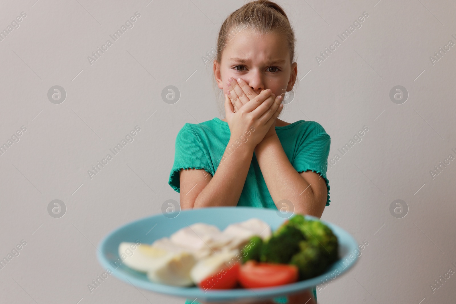 Photo of Cute little girl covering mouth and refusing to eat dinner on grey background