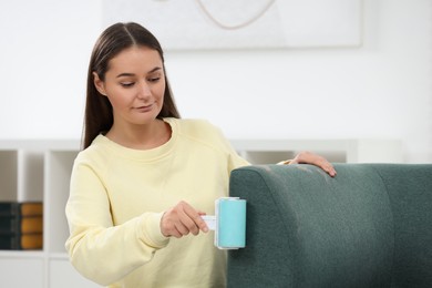 Photo of Woman with lint roller removing pet hair from sofa at home