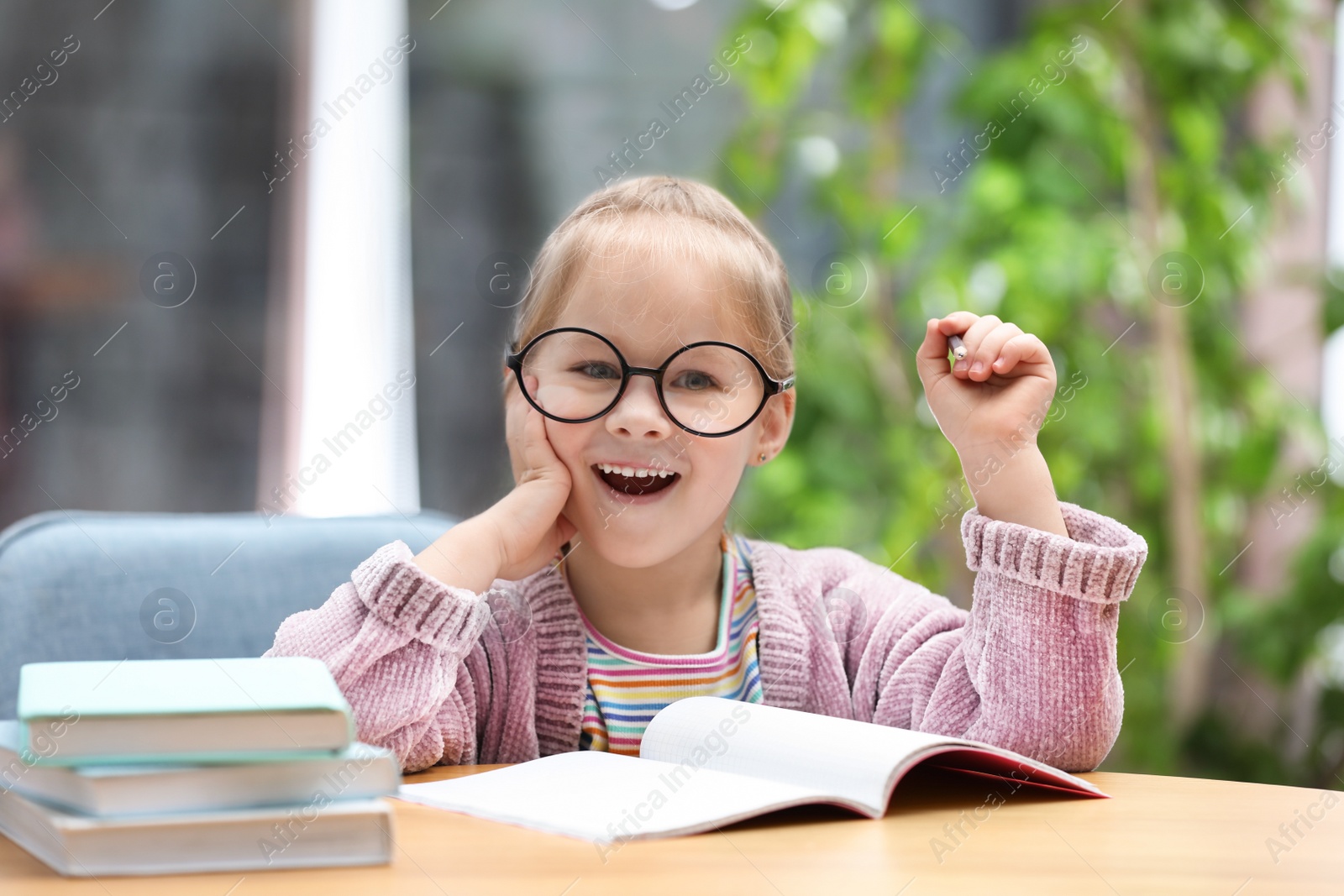 Photo of Cute little girl studying at wooden table indoors