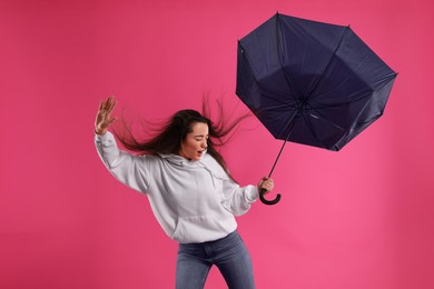 Emotional woman with umbrella caught in gust of wind on pink background