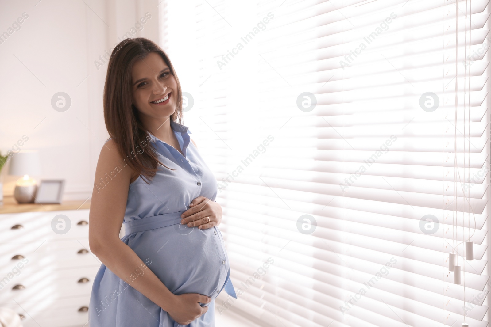 Photo of Young pregnant woman near window at home, space for text