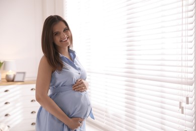 Photo of Young pregnant woman near window at home, space for text